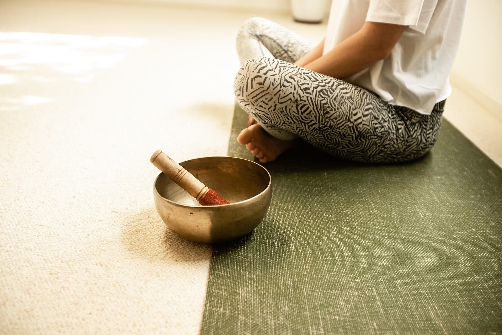 Calm wellness scene — a person seated on a green yoga mat beside a Tibetan singing bowl