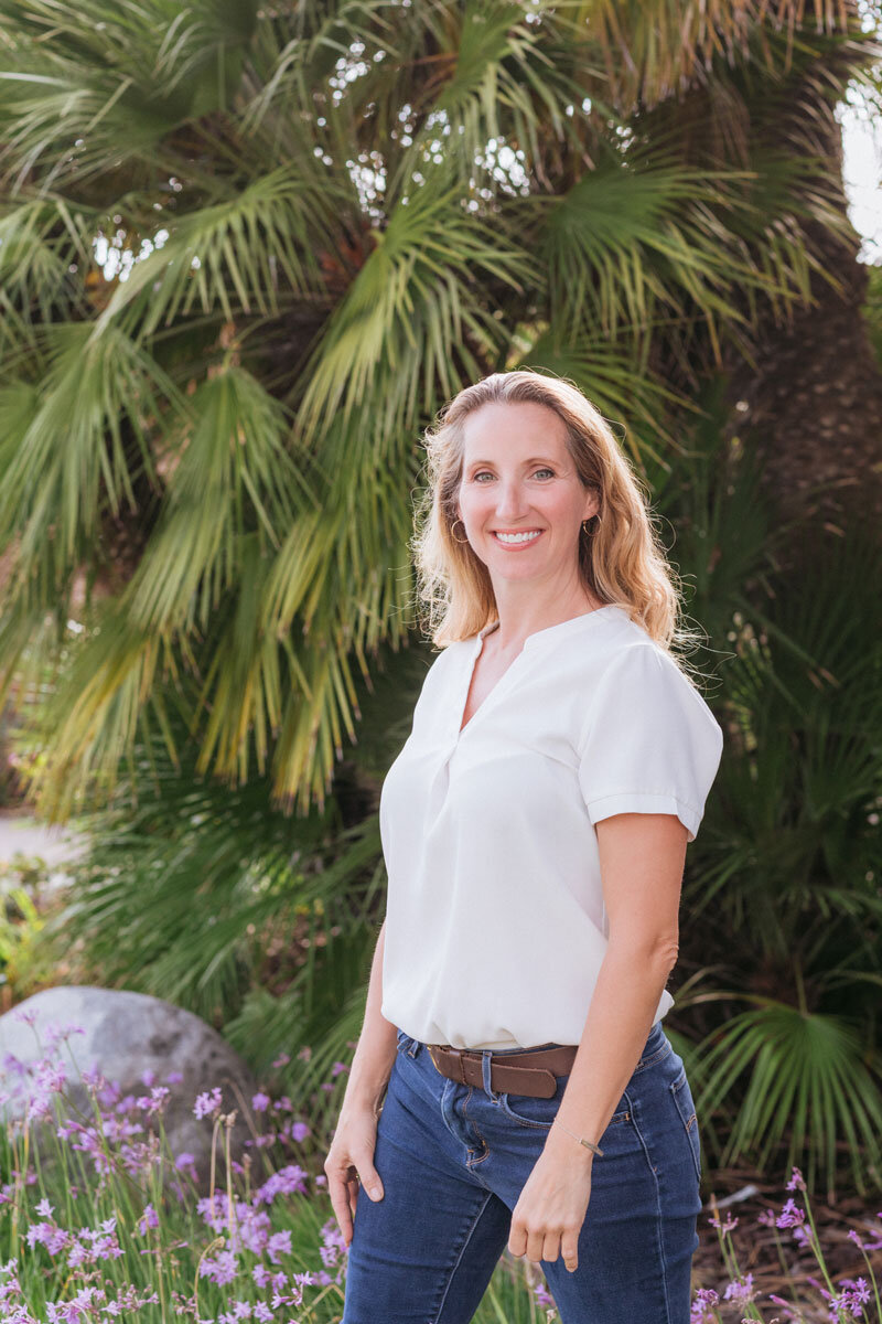 On Point owner Melissa Lone standing outdoors among palms and purple flowers