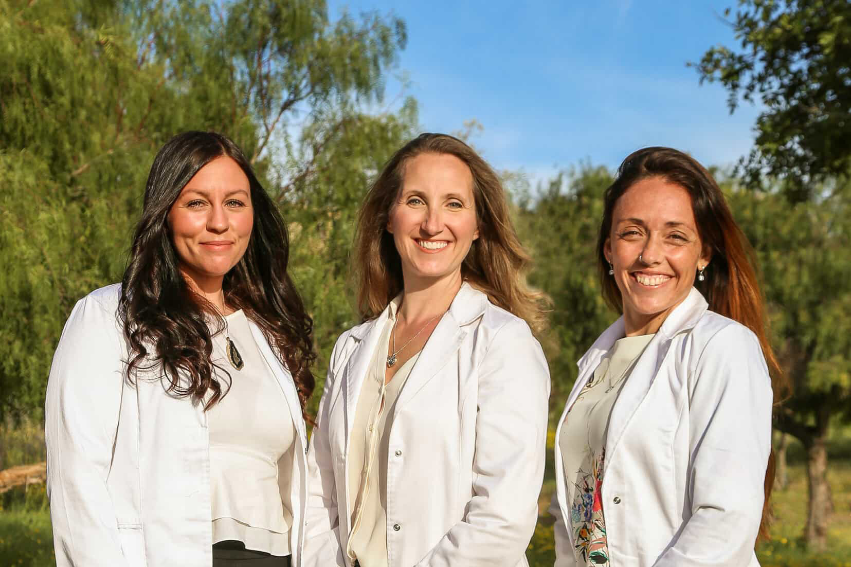 Three On Point practitioners in white coats standing together outdoors under a clear blue sky
